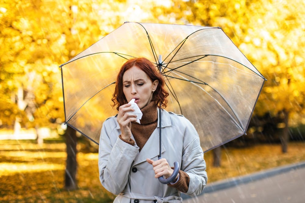 A woman holding on to the umbrella and coughing 